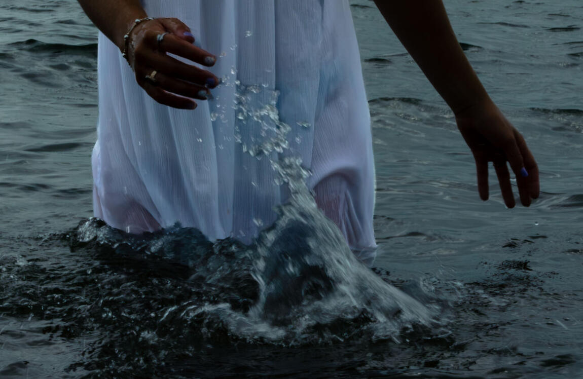Water falling down the front of a white dress, both hands open