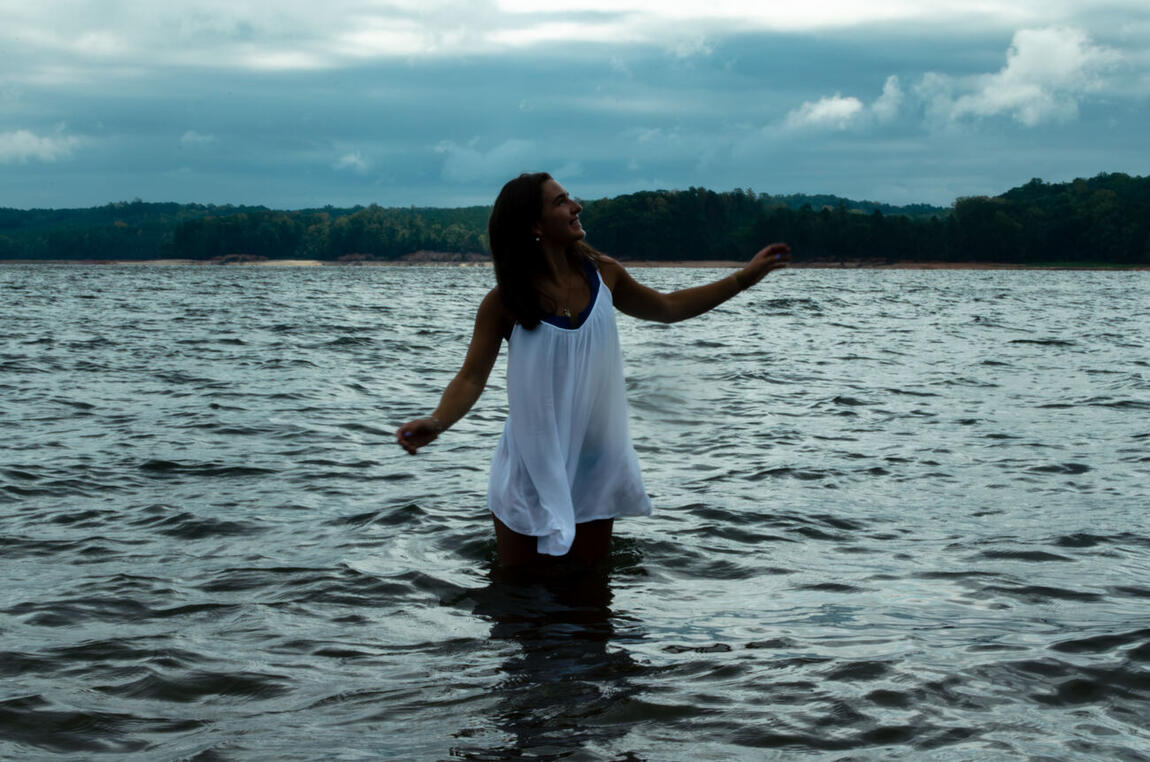 A figure in a white dress turning and laughing, waist-deep in the lake